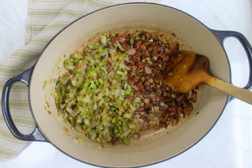 Fully browned bacon in a soup pot cooked along side onion and celery.