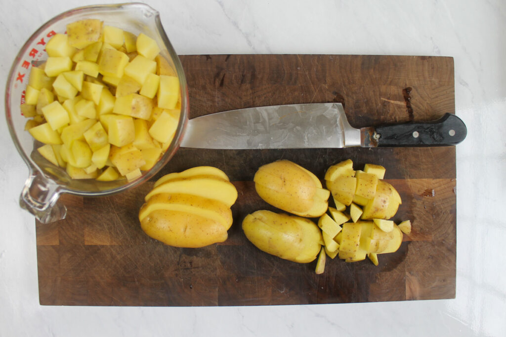 Chopped potatoes on a cutting board, measured in glass pyrex measuring cup.