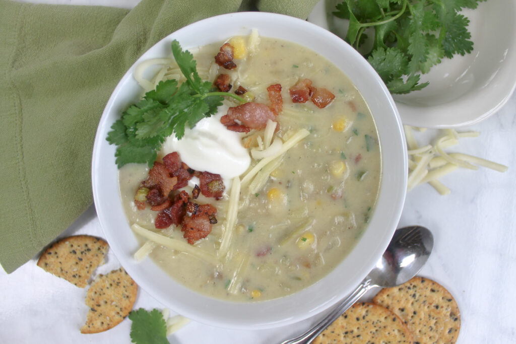 A bowl of potato corn chowder with toppings and multigrain crackers.