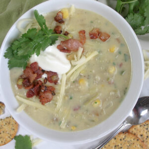 A bowl of potato corn chowder soup with cilantro, cheese, plain yogurt and crumbled bacon.