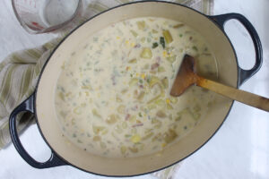 Pot of potato corn chowder ready to be mashed with a potato masher.