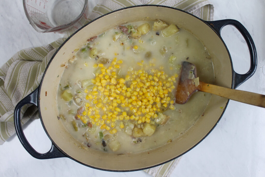 Adding frozen corn to a pot of potato corn chowder.