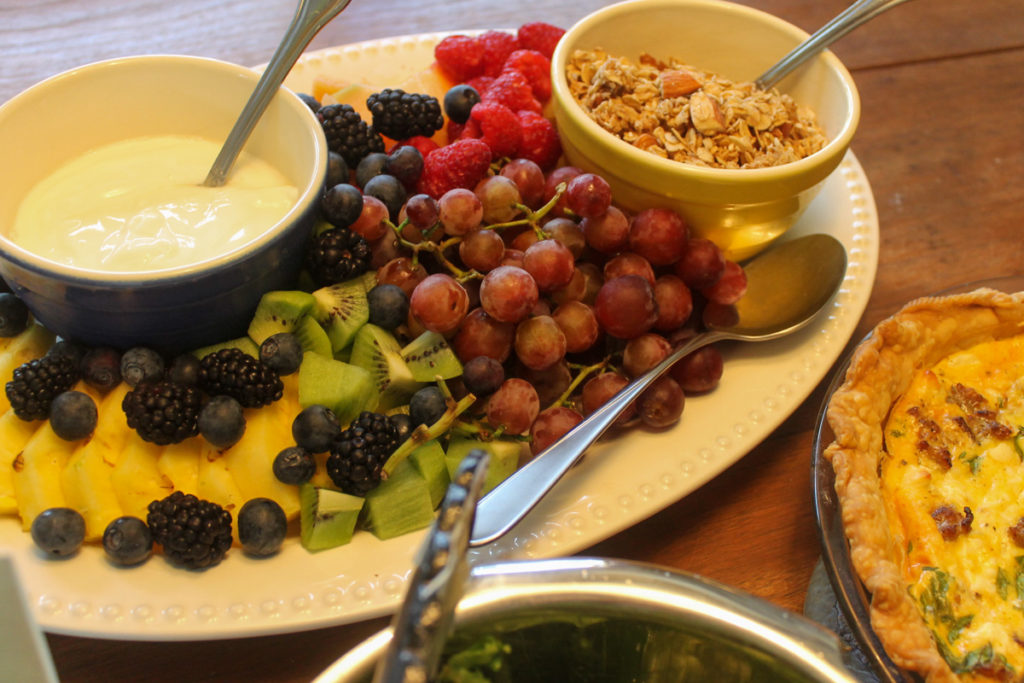 A cut fruit platter with a bowl of yogurt and a bowl of granola.