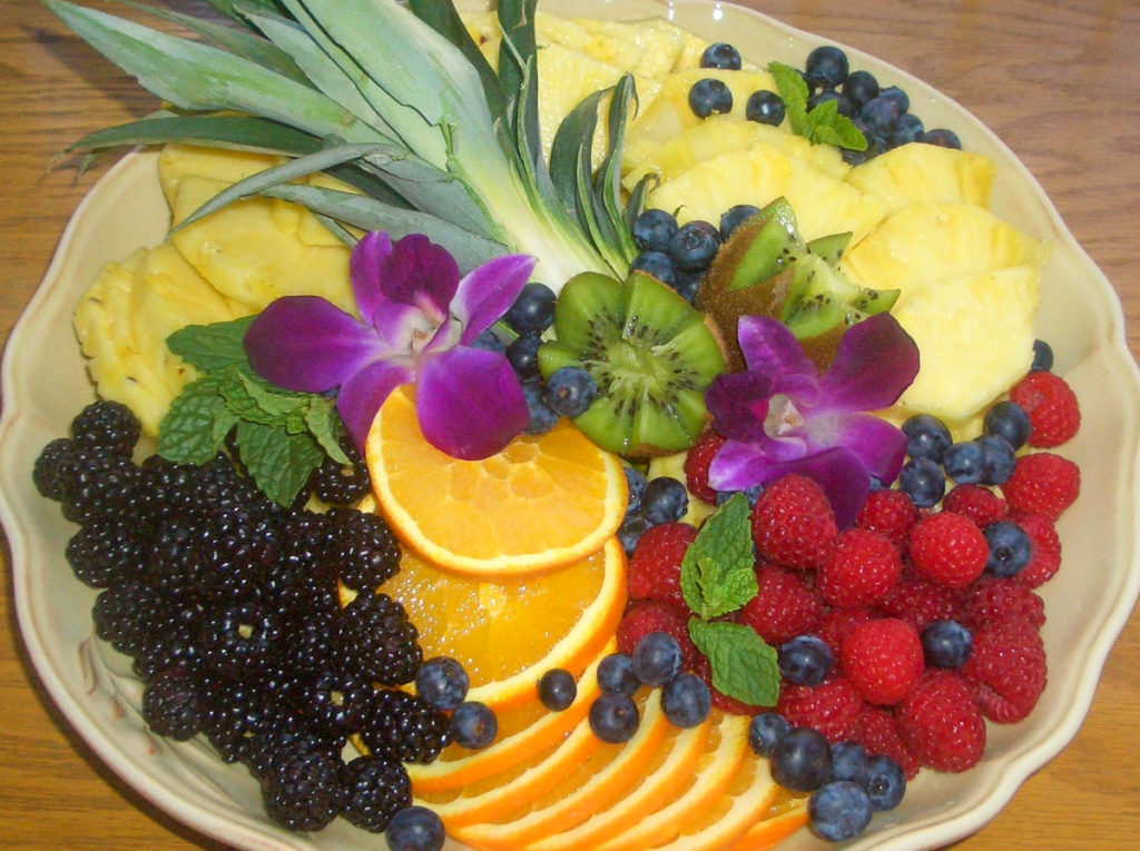 A beautiful fruit platter with pineapple, blackberry, kiwi and edible flowers.