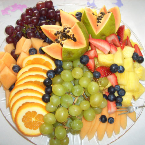 Fruit platter presentation with pineapple, grapes, papaya, and oranges.