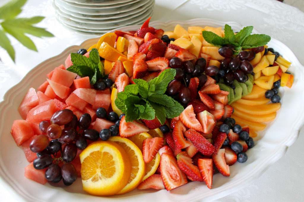 Making a fruit tray for a party brunch with watermelon, oranges, grapes, berries, and mint leaves.