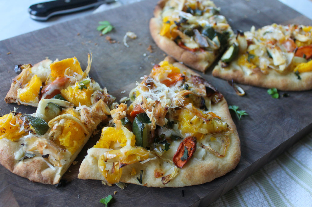 Vegetarian flatbread pizza sliced on a cutting board.