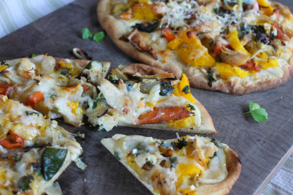 Chicken and vegetable flatbread pizza sliced on a board.