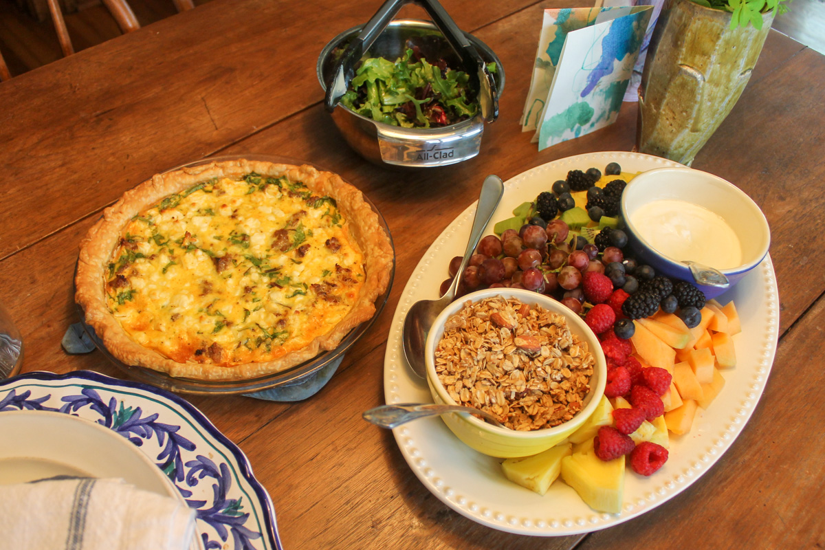 A table set for brunch with quiche, salad, and fruit with yogurt and granola.