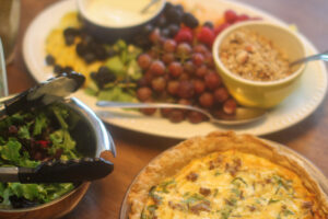 A sausage spinach quiche, bowl of salad and platter of fruit for brunch.