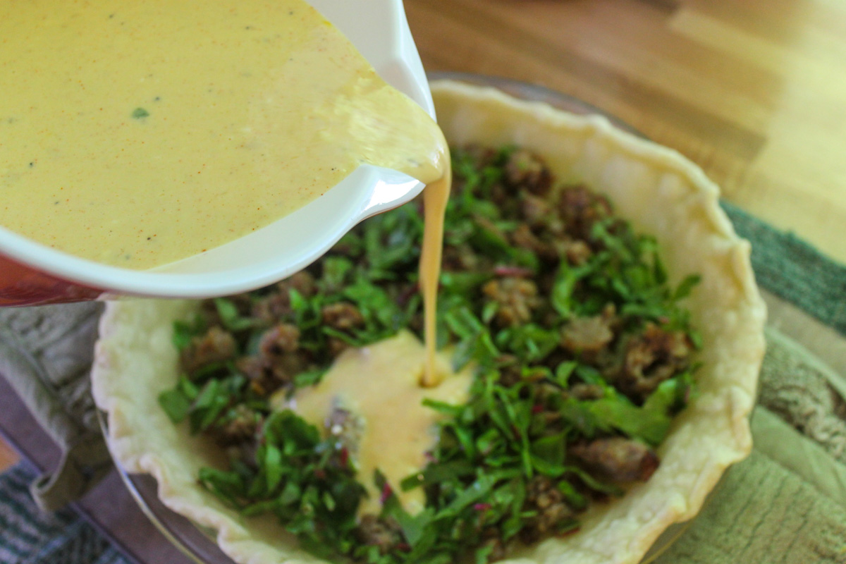 Pouring egg mixture into a quiche pie crust with filling.