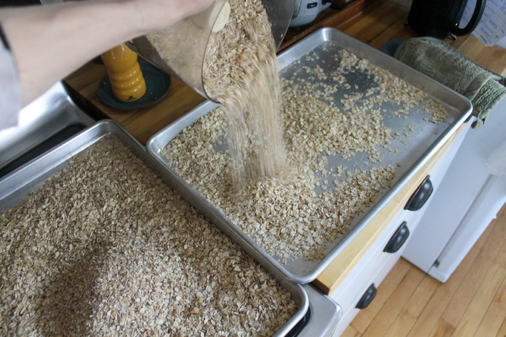 Pouring the ground oats, nuts, and seeds bake in with the regular rolled oats on large sheet pans.