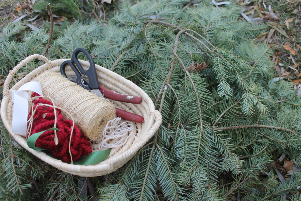 A basket of wreath making supplies sitting on a pile of pine branches.