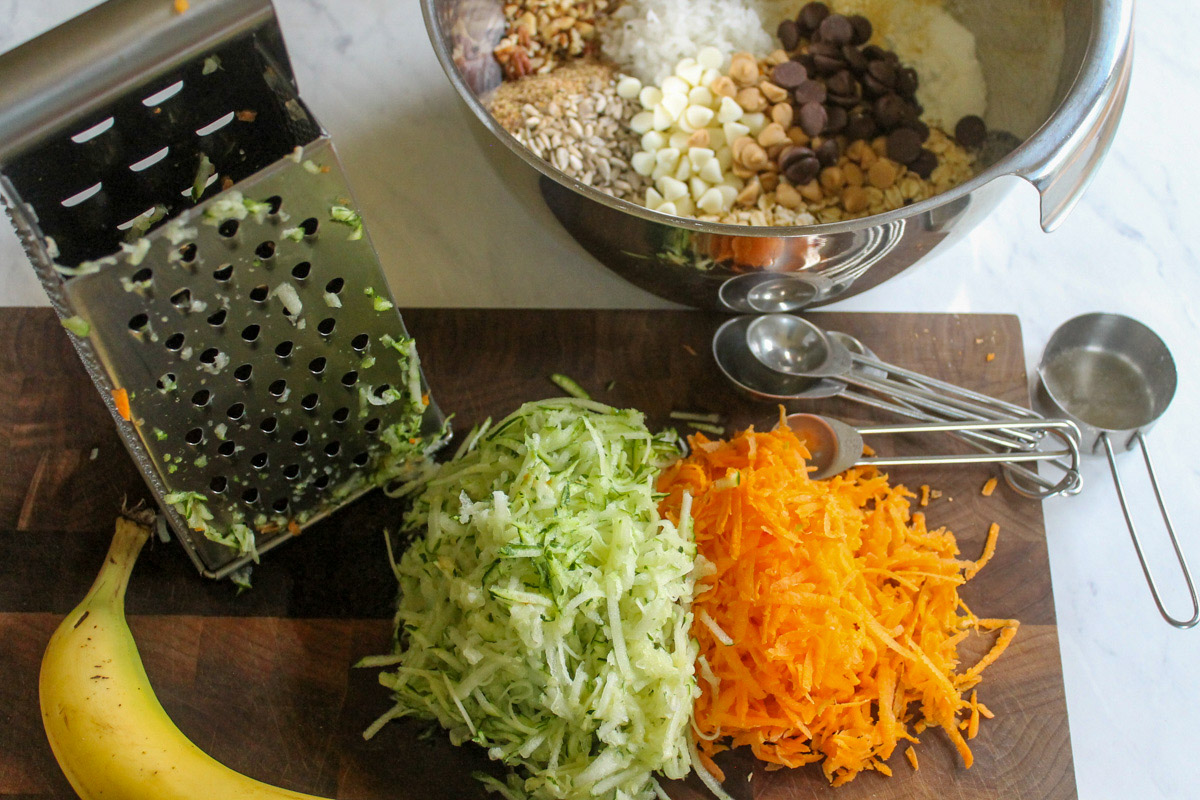 Healthy zucchini banana cookies ingredients on a cutting board, shredded zucchini and carrots.