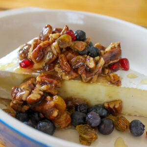 A wedge of brie with fruit honey and nut topping.
