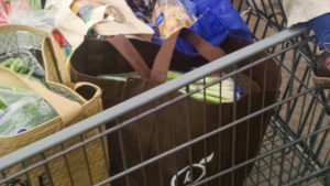A shopping cart full of groceries in reusable cloth bags.