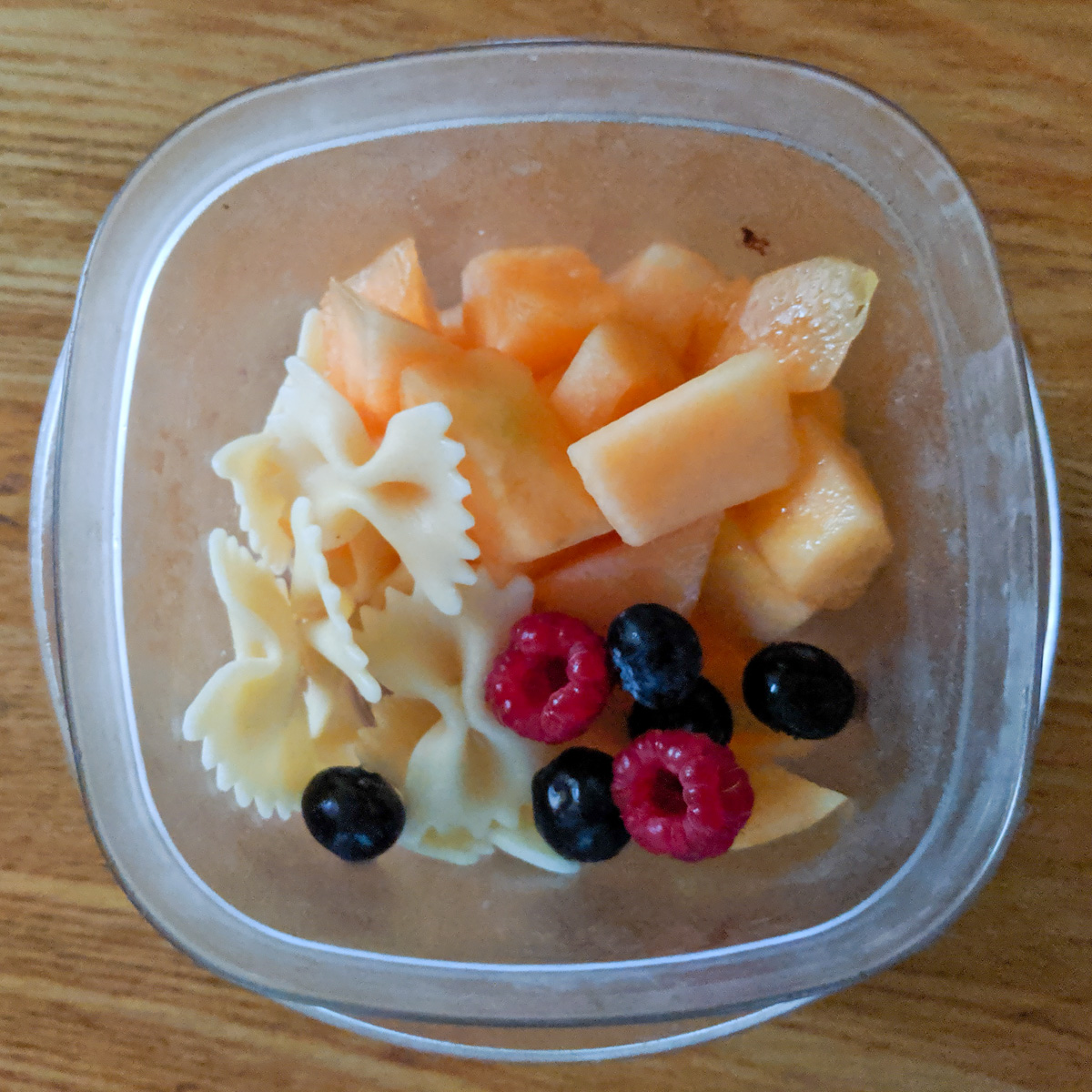 A snack cup with bowtie pasta, cantaloupe, and berries.