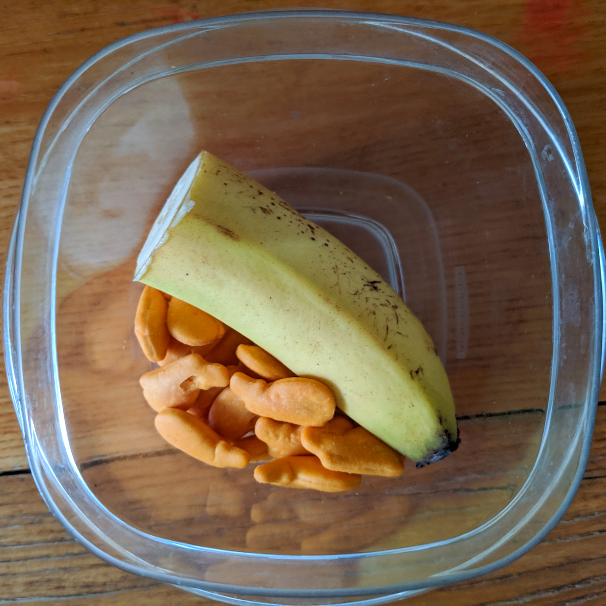 A cup with half a banana and goldfish crackers.