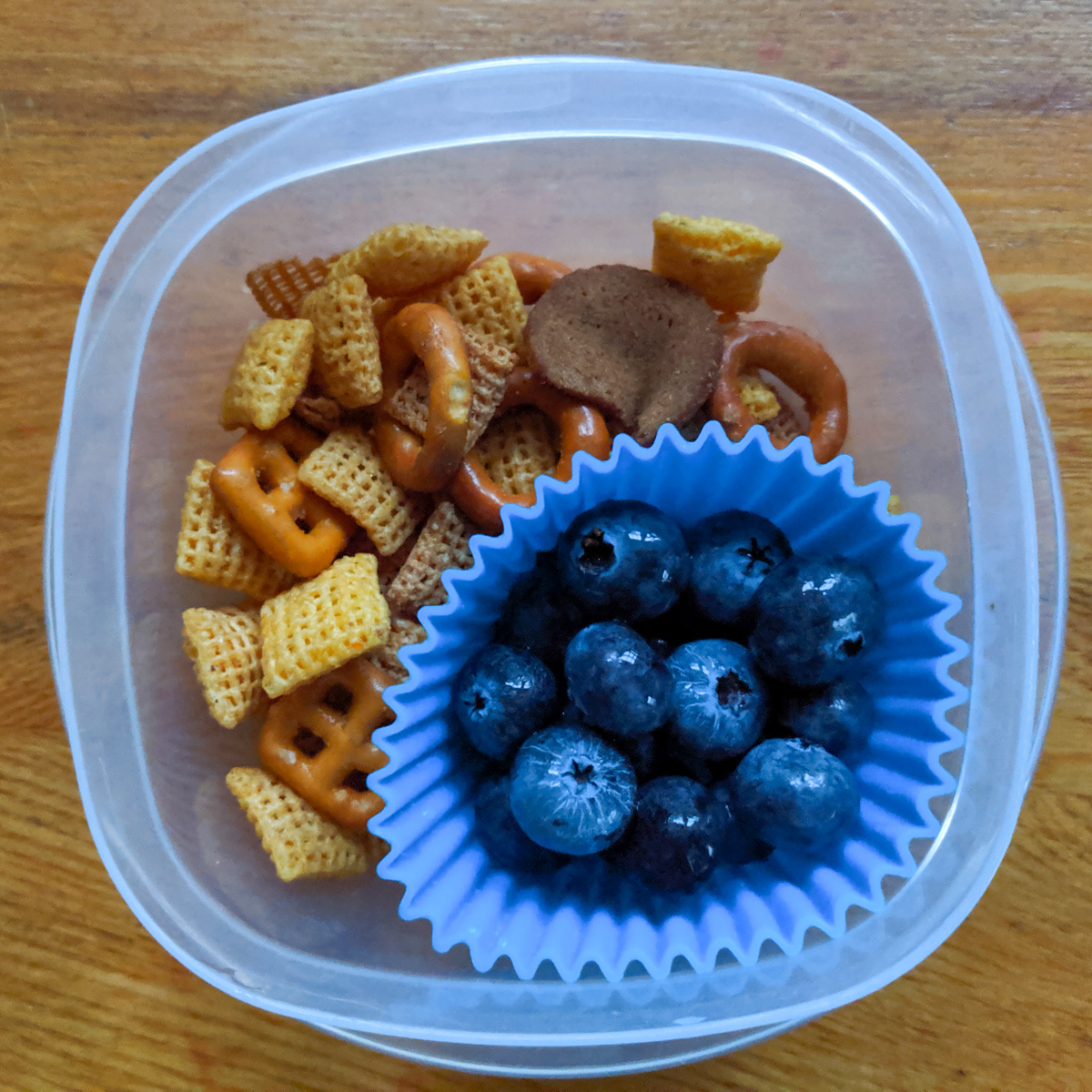 A cup of chex mix and fresh blueberries in a silicone muffin cup to keep it separated.