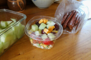 A bag of beef sticks, a container of melon and a healthy snack cup to go for kids.