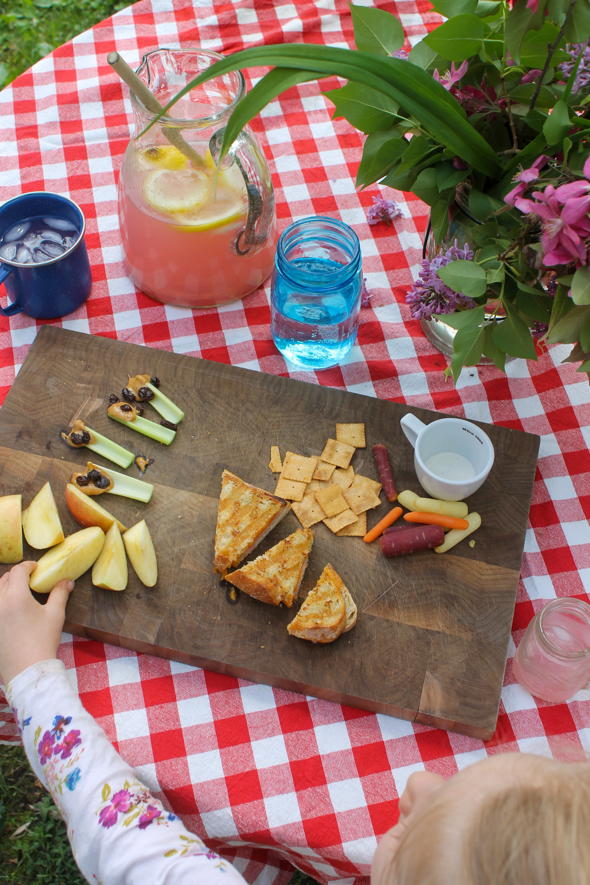 An outdoor patio lunch with a cutting board of panini sandwiches, snacks and lemonade.