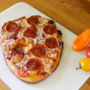 A flatbread pepperoni pizza on a cutting board next to mini peppers.