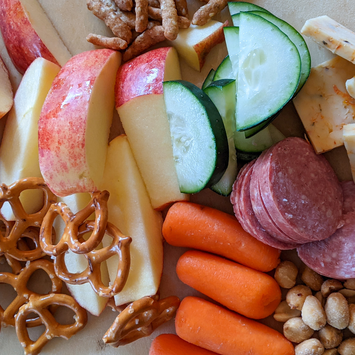 A snack board for a kid's easy lunch with meat and cheese, veggies, pretzels and nuts.