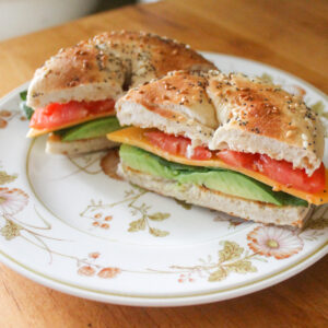 A simple veggie bagel sandwich with avocado, cheese and tomato.