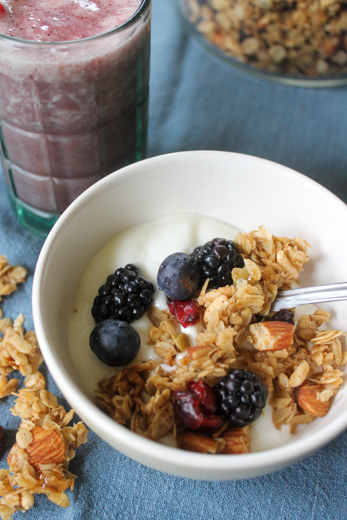 A kid's small bowl of yogurt with homemade granola and berries next to a smoothie.
