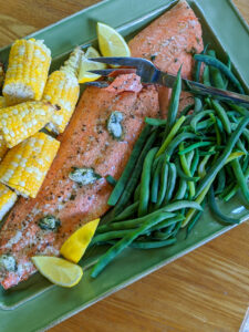 A platter of roasted salmon with kid friendly side dishes like blanched green beans and corn on the cob.
