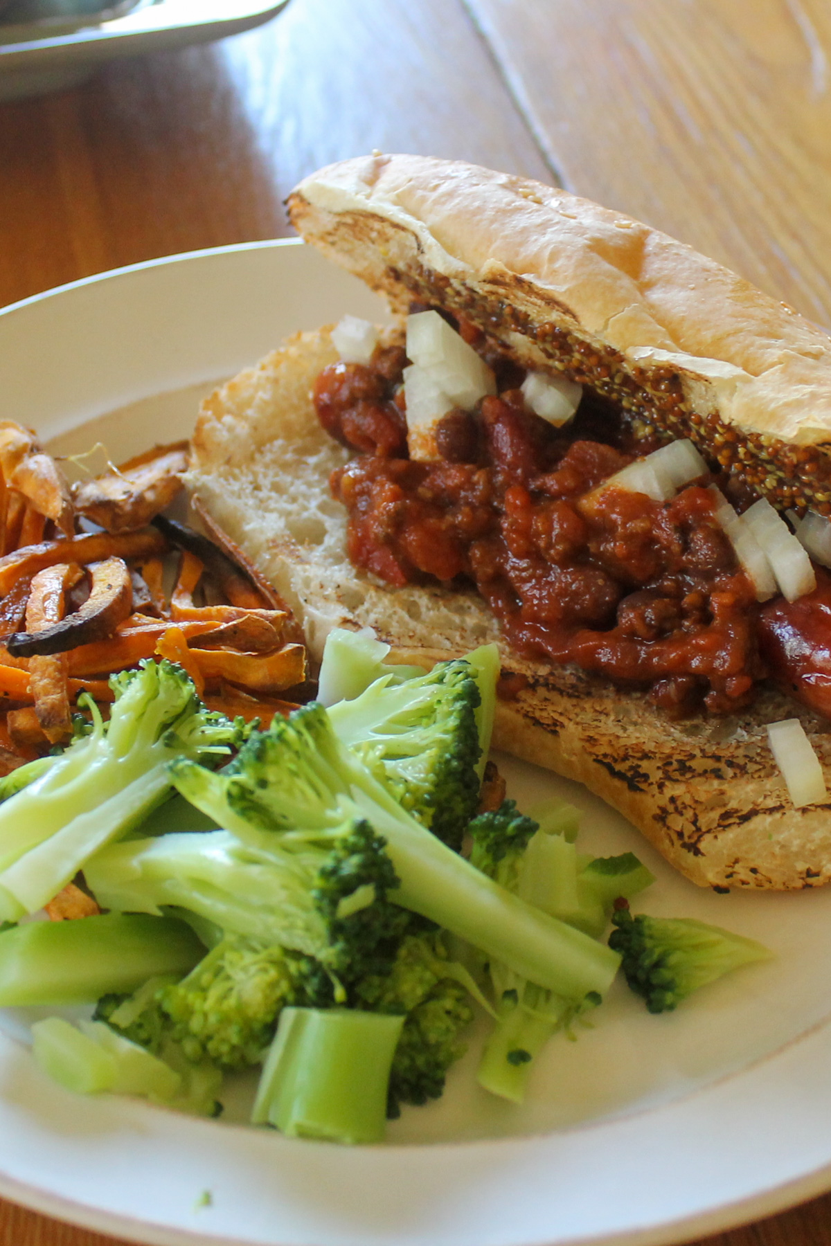 Buttered broccoli, quickly blanched in boiling water on a plate with oven fries and a chili dog.