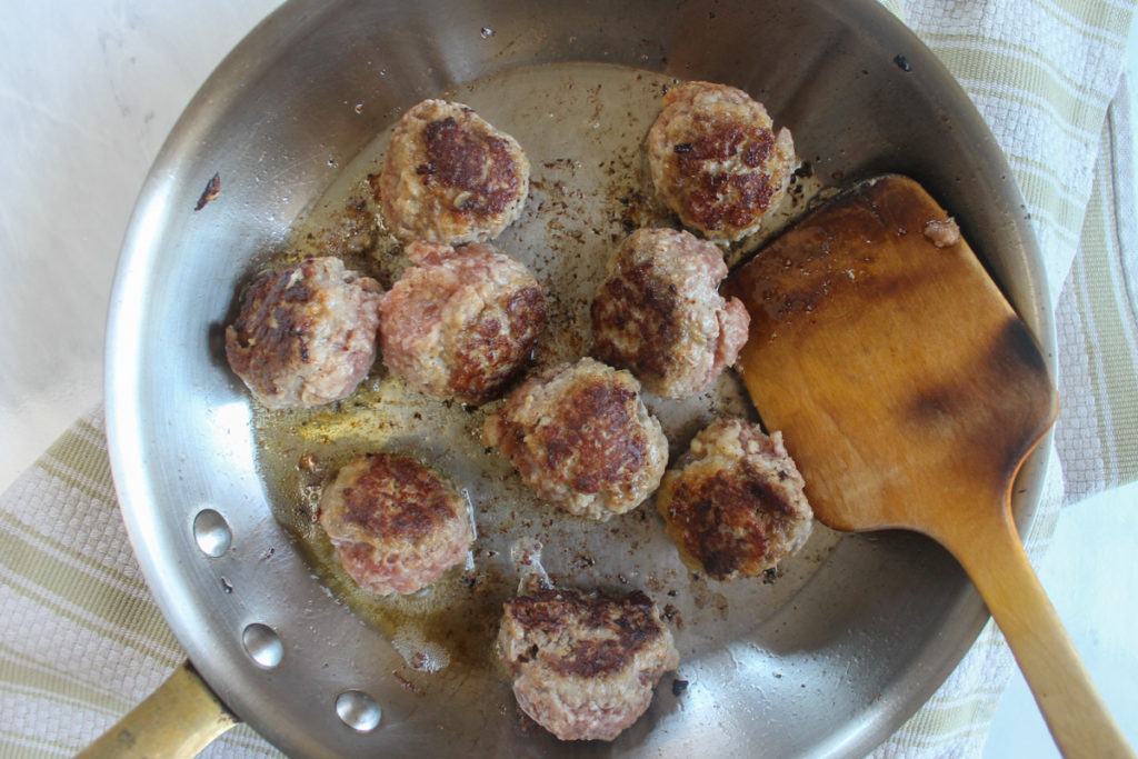 Searing meatballs in a skillet with a wooden spoon.