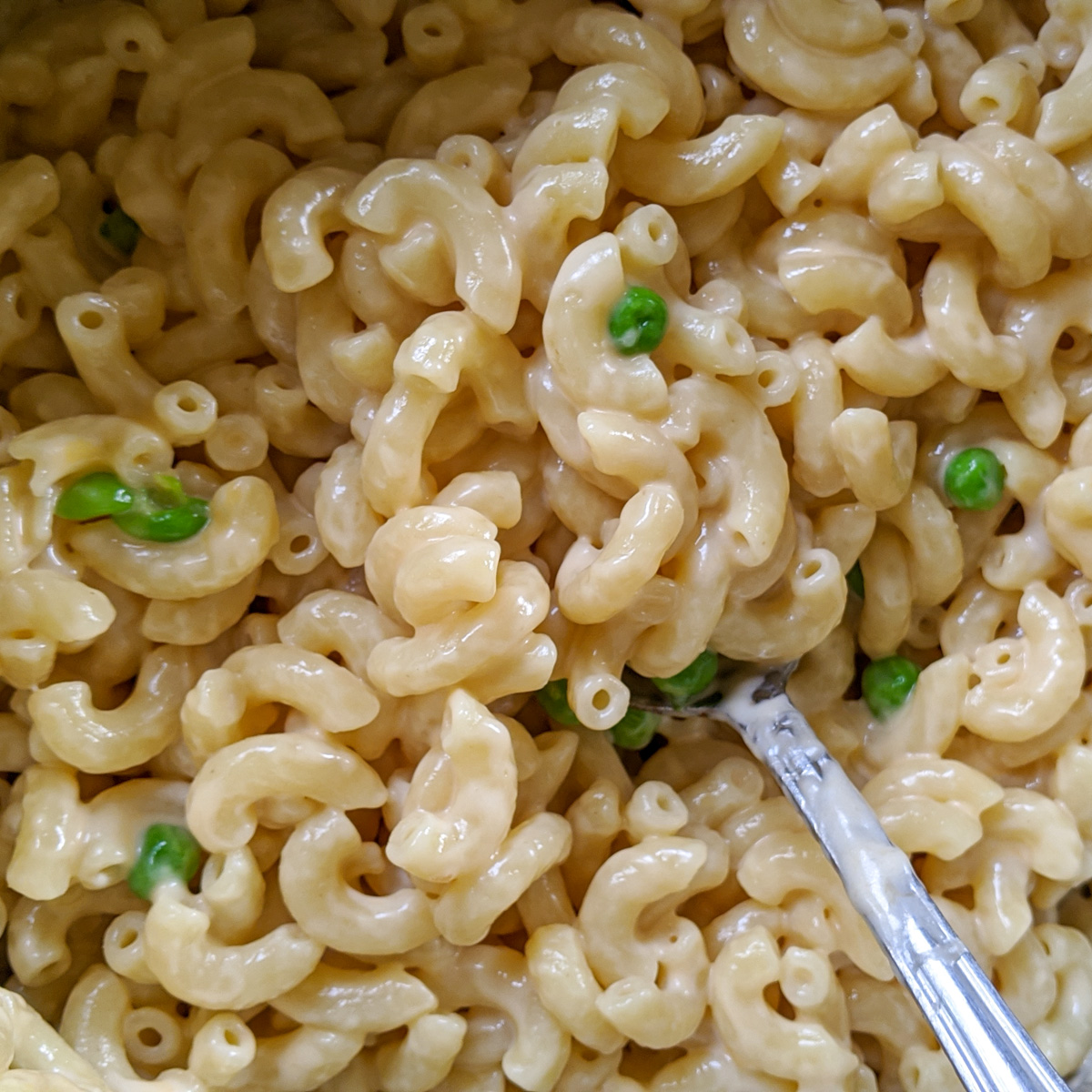 A close up of kids mac and cheese with a few green peas mixed in.