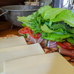 Italian Subs being made, piled with prosciutto, giardiniera and greens.