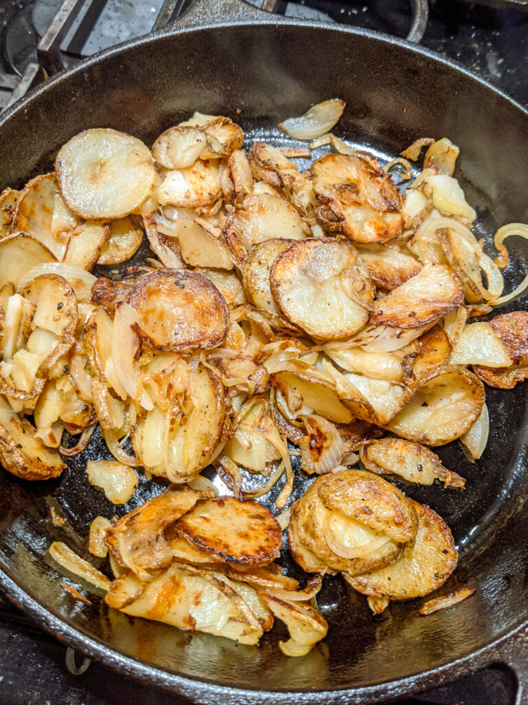 Sliced potatoes and onions fried in a cast iron skillet.