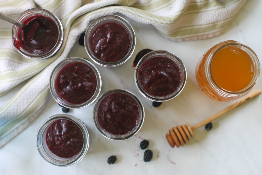 Six small jars of mulberry freezer jam and a jar of honey.