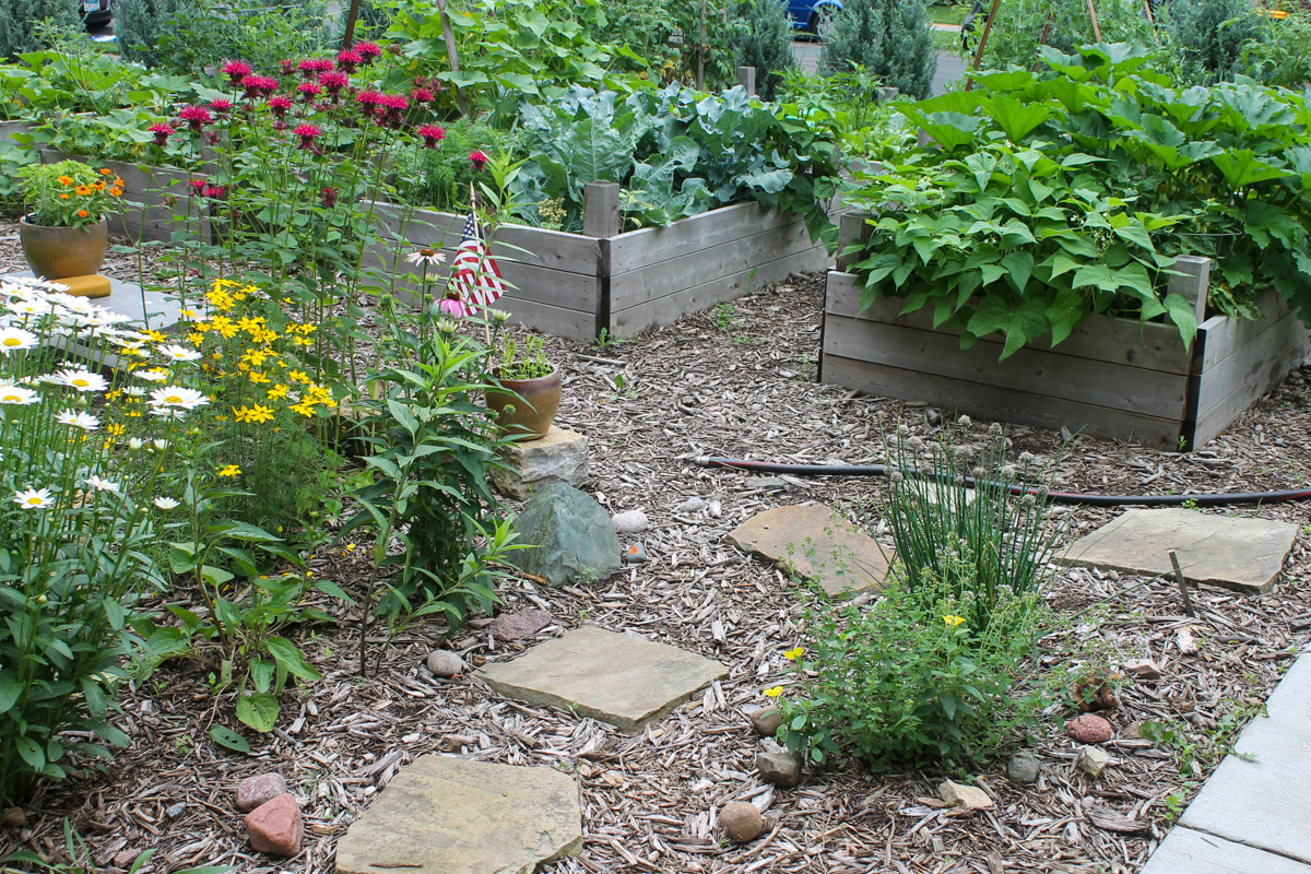A flagstone path with flowers and herbs leading to raised bed vegetable gardens.