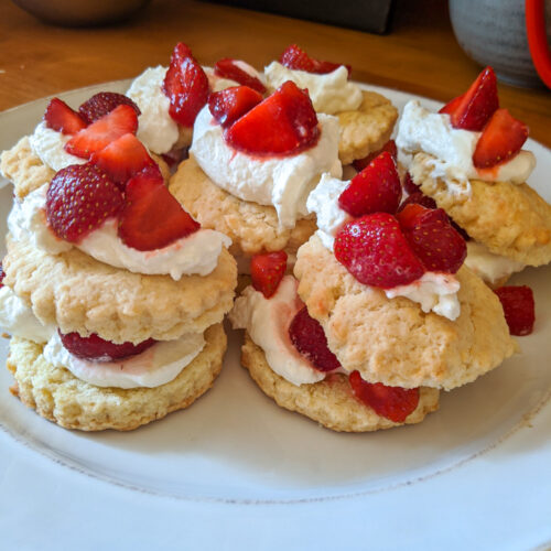 Several assembled strawberry shortcakes layered with whipped cream and strawberries on a white plate.