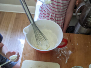 Kids helping to make homemade whipped cream in a bowl with a whisk.