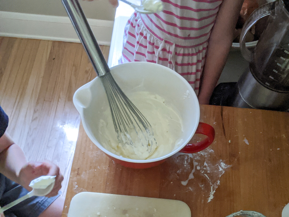 Kids helping to make homemade whipped cream in a bowl with a whisk.