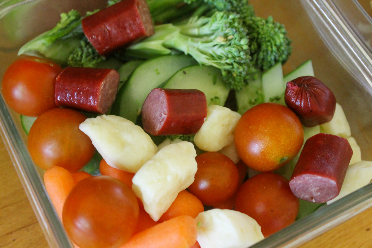 A container of snacks fresh from the garden including cherry tomato, cucumber, and broccoli.