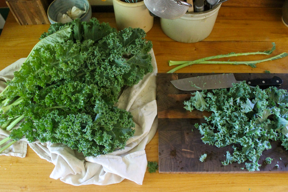 A pile of kale on the counter top and chopping it on a cutting board.
