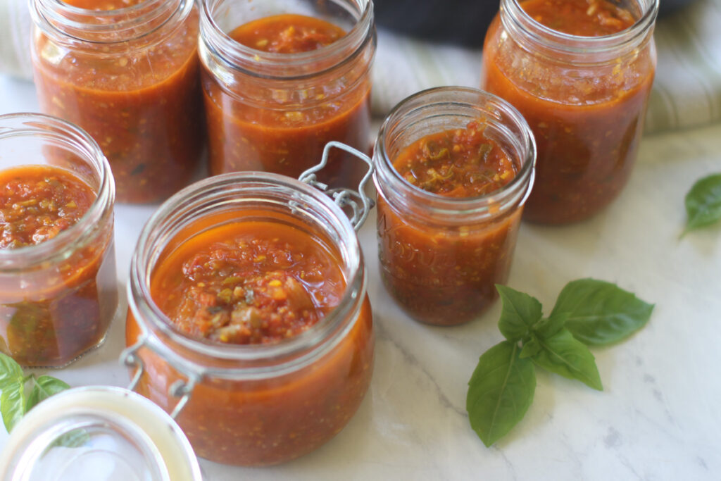 Jars of freezer tomato sauce with fresh basil.