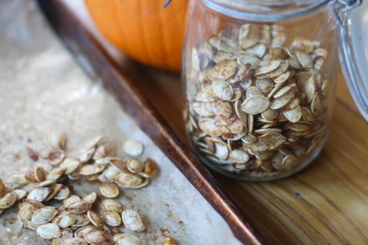 A jar of Roasted Pumpkin Seeds with an orange pumpkin behind it.