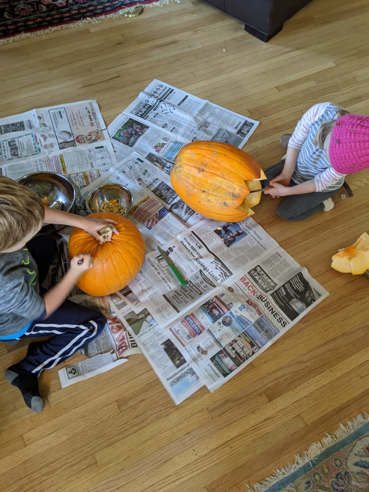 Kids carving pumpkins on newspaper on the floor.