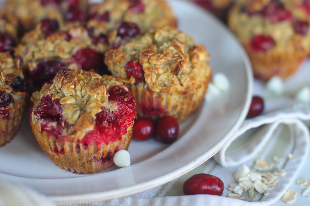 A white plate of cranberry baked oatmeal cups on a towel with white chocolate chips.