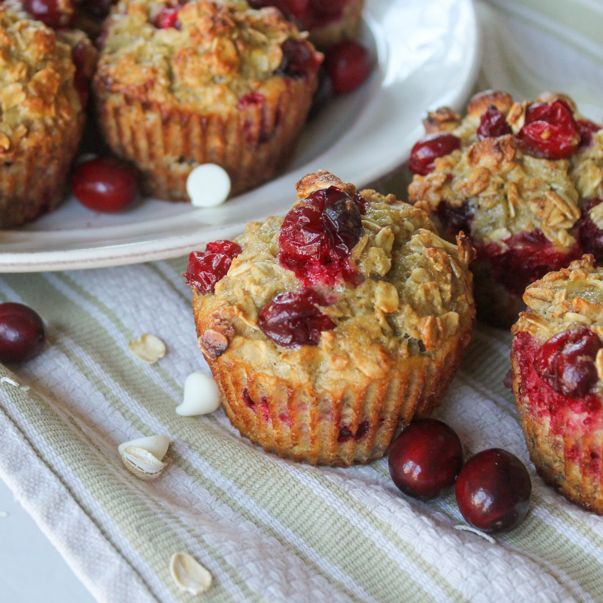 A few cranberry oatmeal cups on a towel in front of a white plate with more.