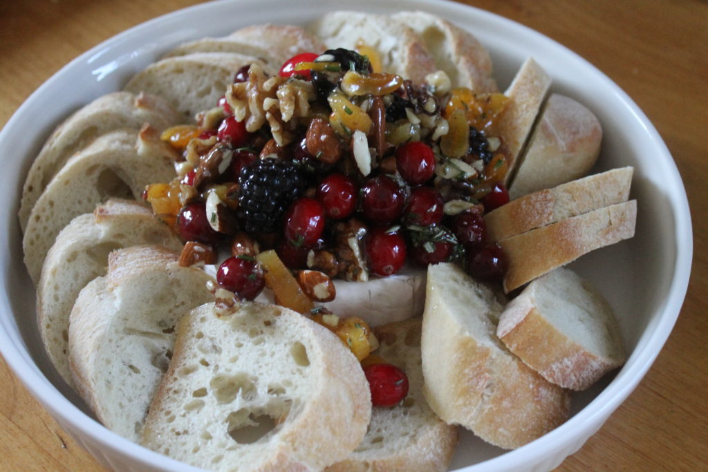 Prebaked Cranberry Honey Baked Brie in a white round dish surrounded with bread, ready for the oven.