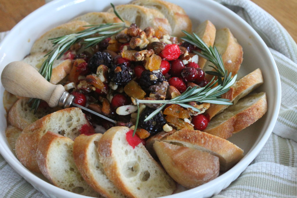 Cranberry Honey Baked Brie hot from the oven with baguette slices and a small serving knife.