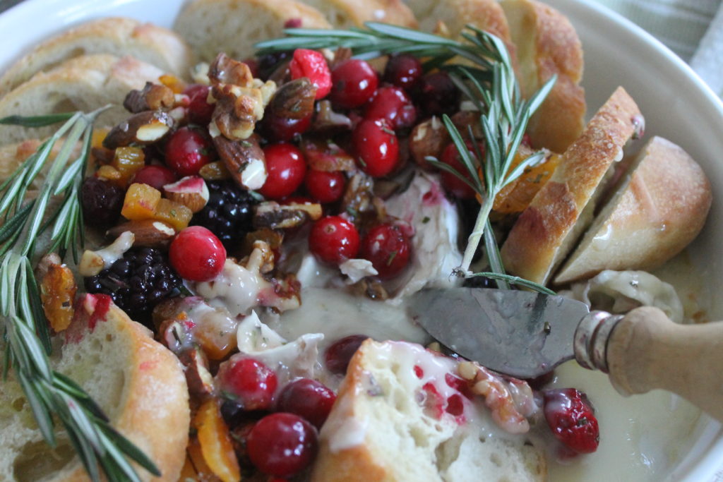 Cranberry Honey Baked Brie with a serving knife in the gooey cheese and bread to dip.